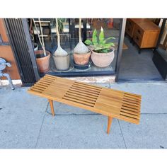 a wooden bench sitting on top of a sidewalk next to potted plants and windows