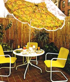 a table with two chairs and an umbrella over it on a brick patio in front of a bamboo fence