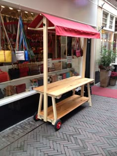 a wooden bench sitting in front of a store window with red awning over it