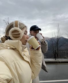 a woman drinking from a coffee cup while standing next to a man on the street