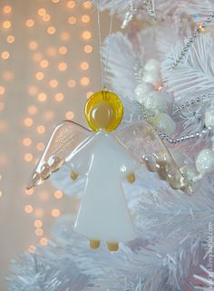 an angel ornament hanging from a white christmas tree with lights in the background