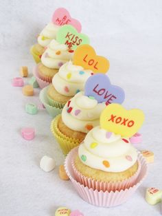 several cupcakes are lined up in rows with hearts on top and candy scattered around them