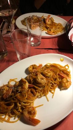 two white plates topped with pasta and shrimp on top of a red cloth covered table