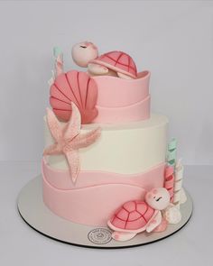 there is a pink and white cake with sea animals on the bottom tier, along with seashells