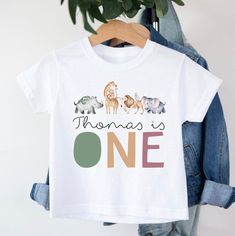 Personalised First Birthday Safari T-shirt T-shirt is 100% cotton.  We design & print our products with care & love! We use the best quality vinyls, inks & transfers on all products. * * * * * * * * * * * * * * * * * * * * * * * * * * * * * CARE INSTRUCTIONS: Wash inside out on gentle wash, Do not tumble dry. * * * * * * * * * * * * * * * * * * * * * * * * * * * * * SHIPPING: We want to get your product to you as quickly as possible, your purchase will be shipped through Australia post, Express post is available for selection. * * * * * * * * * * * * * * * * * * * * * * * * * * * * * GUARANTEE: We stand behind our products with a 100% guarantee; if you are unsatisfied with our product, please let us know & we will rectify any issues. We are unable to refund products due to change of mind o Graphic Tee With Name Print For Birthday Gift, Cotton Crew Neck T-shirt As Birthday Gift, Fun Cotton T-shirt For Birthday Gift, White Character Print Top For Birthday Gift, White Cartoon Print Top As Birthday Gift, Graphic Cotton Tee For Birthday, Cotton T-shirt With Graphic Print For Birthday Gift, Graphic Cotton T-shirt For Birthday Gift, Cotton Graphic Print T-shirt For Birthday Gift