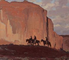 two men on horses are riding in front of a large rock