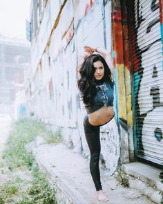 a woman in black leggings leaning up against a wall with graffiti on it