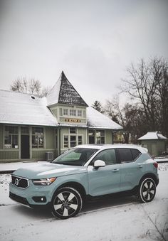 a light blue car parked in front of a building with snow on the ground and trees