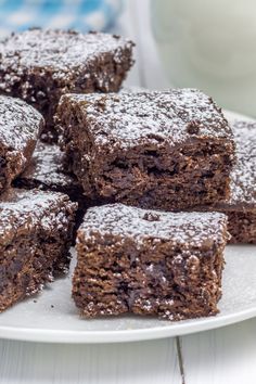 several pieces of brownie on a plate with powdered sugar and milk in the background