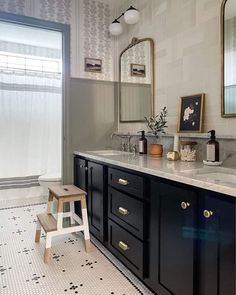 a bathroom with black cabinets and white tile on the floor, along with two stools