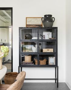 a black bookcase with baskets and vases on it in a living room area