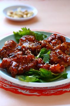 a white plate topped with meat and greens on top of a pink tablecloth covered table