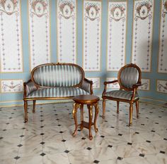 two chairs and a table in front of a wallpapered room with floral designs