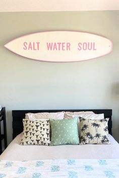 a bedroom with a surfboard above the bed and pillows on the head board that says salt water soul