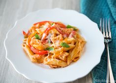 a white plate topped with pasta covered in sauce and vegetables next to a fork on top of a blue towel