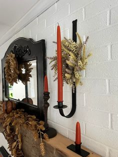 a mirror and some candles are on a mantle in front of a white brick wall