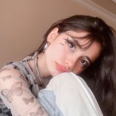 a woman with butterfly tattoos on her face and arm is posing for the camera while wearing a white shirt