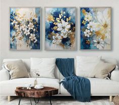 three paintings hanging on the wall above a white couch in a living room with a coffee table