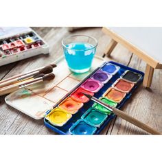 an artist's palette with watercolors and paintbrushes on a wooden table