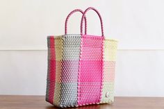 a pink, yellow and white bag sitting on top of a wooden table next to a wall