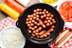 hot dogs in a crock pot on a table with other foods and condiments