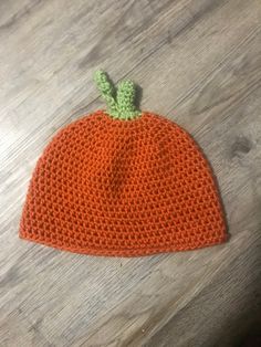 an orange knitted beanie with a green leaf on top sitting on a wooden table