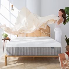 a woman standing next to a bed with a white sheet over it