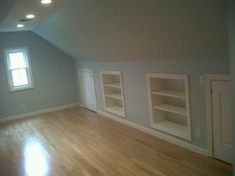 an empty room with wood floors and white bookcases on the far wall in front of two windows