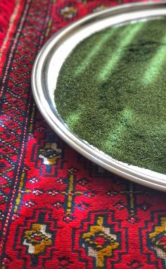 a plate with some green stuff in it on a red table cloth next to a rug