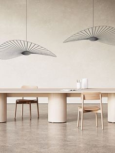 a dining room table with chairs and two hanging lights above it, in front of a white wall