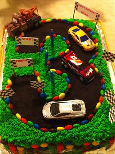 a birthday cake with cars and race flags on it's side, in the shape of a racetrack