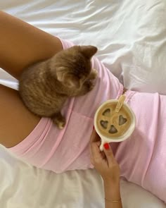 a cat sitting on the belly of a woman holding a cup of coffee in her hand