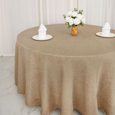 the table is set with two white flowers and napkins on it, along with a gold vase