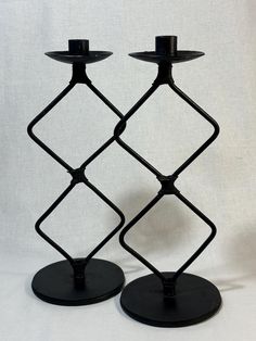 two black candlesticks sitting next to each other on top of a white surface