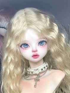 a close up of a doll with blonde hair and blue eyes wearing a choker