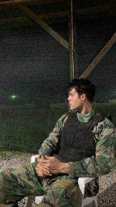 a man in camouflage sitting on a white chair with his legs crossed and looking off into the distance