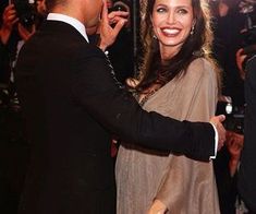 a man in a tuxedo is shaking the hand of a woman who is wearing a brown dress