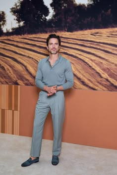 a man standing in front of a painting wearing blue pants and a gray polo shirt