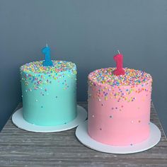 two birthday cakes sitting on top of each other in front of a gray wall and wooden table