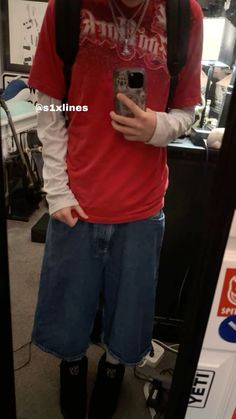 a young man is taking a selfie in the mirror with his cell phone while wearing a red shirt and blue shorts