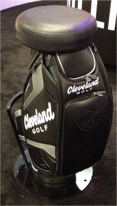 a black golf bag sitting on top of a floor next to a white sign that says cleveland golf