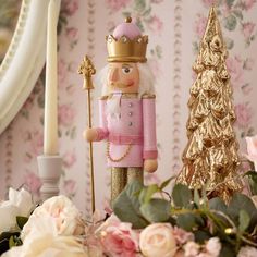 a nutcracker figurine with a pink coat and crown standing next to flowers