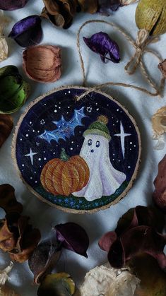 an embroidered decoration with a ghost holding a pumpkin on it's side and leaves surrounding it