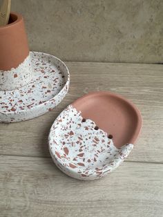 two ceramic dishes with holes in them sitting on a wooden table next to a potted plant