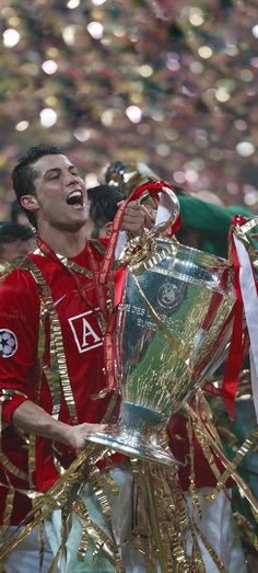 a man in red shirt holding up a silver trophy with other people behind him and confetti around him