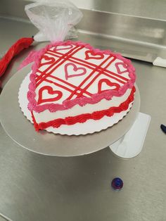 a heart shaped cake with red icing and hearts on it sitting on a table