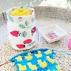 a basket filled with yarn next to a knitted pot holder and knitting kit on top of a wicker table