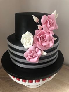 a stack of black and white cakes with pink flowers on each cake plate, sitting on a wooden table