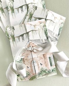 several folded cards with watercolor drawings on them and ribbons tied around the edges, sitting on a table