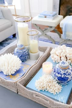 two trays with flowers and candles are on the table in front of a couch